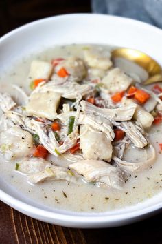 a white bowl filled with chicken and dumplings on top of a wooden table next to a spoon