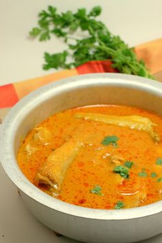 a white bowl filled with soup on top of a wooden table next to parsley