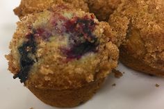 three blueberry muffins sitting on top of a white plate with crumbs