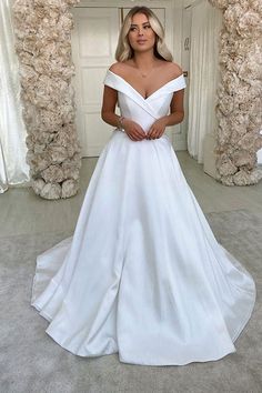 a woman standing in front of a mirror wearing a white wedding dress with off the shoulder sleeves