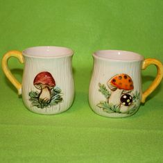 two coffee mugs with mushrooms painted on them are sitting side - by - side