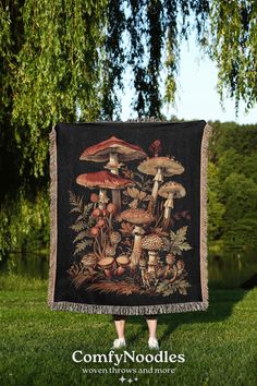 a woman standing in the grass holding up a tapestry with mushrooms and leaves on it