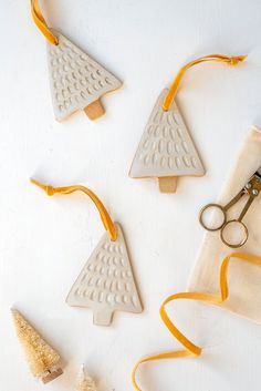 four ceramic christmas trees with yellow ribbon and scissors on a white surface next to each other