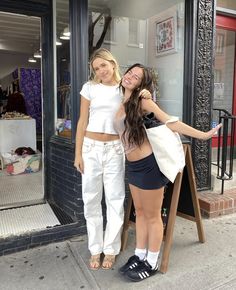 two women standing in front of a clothing store posing for the camera with their arms around each other