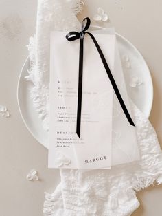 a white plate topped with a piece of paper next to a black ribbon tied around it