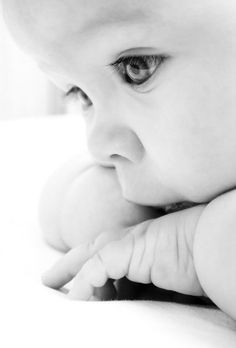 a black and white photo of a baby's face with its hand on the cheek