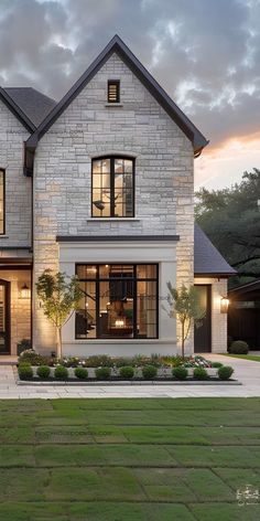 a large white brick house with lots of windows and plants in the front yard at dusk