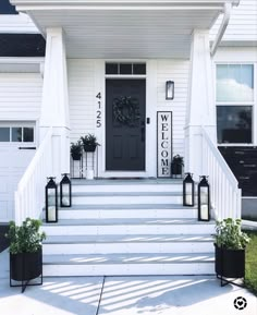 the front steps of a white house with black planters and welcome sign on it