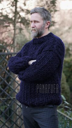 a man with a beard wearing a blue sweater standing in front of a chain link fence