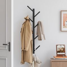 a coat rack with coats hanging on it next to a wooden table and white wall