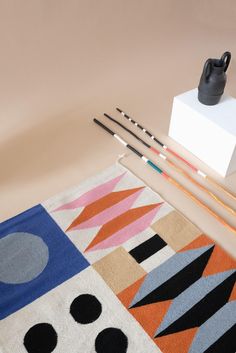 an assortment of knitting needles on top of a rug next to a small black vase