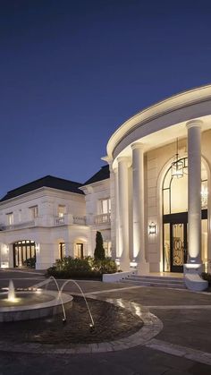 a large white building with a fountain in front of it at night, lit up by lights