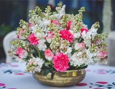 pink and white carnations in a gold bowl on a table with red and white flowers