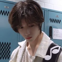 a male in a black and white sweater is looking at his cell phone while standing next to lockers