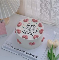 a birthday cake decorated with pink and white icing on a table next to flowers