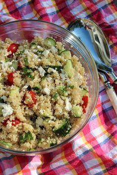 a bowl filled with rice and vegetables on top of a checkered table cloth next to a spoon