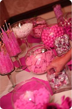 a table topped with lots of candy covered in pink and white candies next to wine glasses