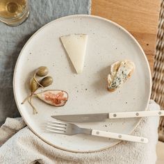 a white plate topped with cheese and olives next to a glass of wine on top of a table