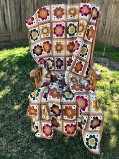 a crocheted blanket sitting on top of a wooden chair in the grass next to a fence