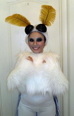 a woman in a white costume with yellow feathers on her head and black eyeliners