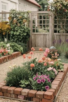 a garden filled with lots of flowers next to a wooden fence on top of a gravel road