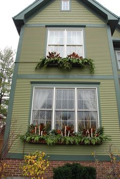 a green house with flowers and greenery in the window boxes on the second floor