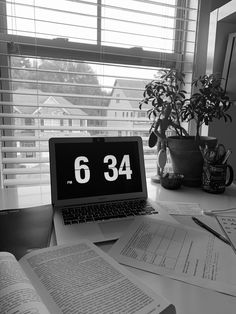 an open laptop computer sitting on top of a desk next to books and plants in front of a window