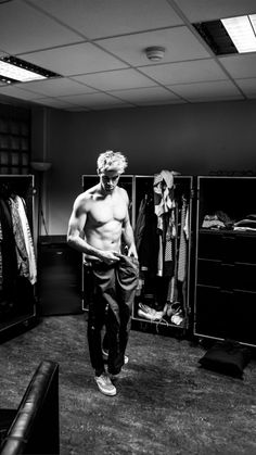 a shirtless man is looking at his cell phone in the dressing room while standing next to some closets