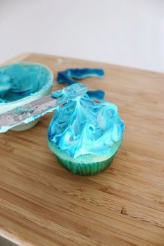 a cupcake with blue icing sitting on top of a wooden cutting board next to a knife