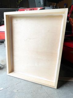 a wooden frame sitting on top of a table next to a red object in the background