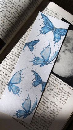 an open book with blue butterflies on it and the moon in the distance behind it