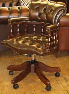 a green leather office chair sitting on top of a wooden floor next to brown leather couches