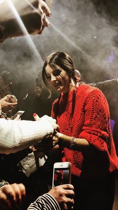 a woman in a red sweater signing autographs for someone on her cell phone at an event