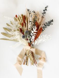 an arrangement of dried flowers and leaves on a white background with ribbon tied around it