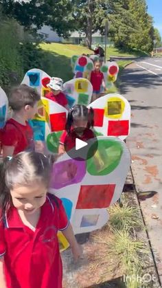 children are standing in front of colorful sculptures on the side of the road and one girl is holding her hand out