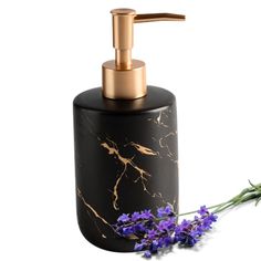 a black soap dispenser with gold accents and purple flowers next to it