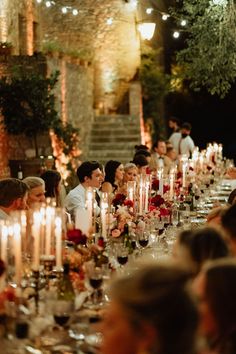 a group of people sitting around a long table with candles on it and plates in front of them