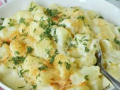 a white bowl filled with potatoes covered in gravy and garnished with herbs