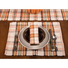 a place setting with silverware and plaid napkins on a wooden dining table, pumpkin in the background