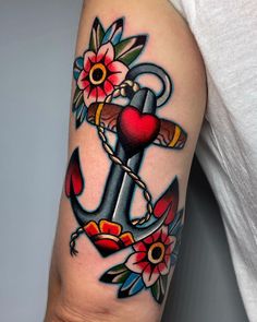 an anchor with flowers on it and a heart in the middle is tattooed onto someone's arm