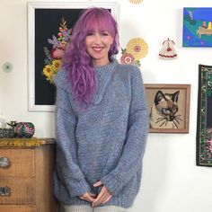 a woman with purple hair is standing in front of a wall full of pictures and paintings