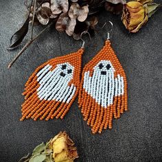 an orange and white beaded pair of earrings on top of a table next to dried flowers