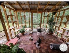 the inside of a wooden house with lots of windows and plants on the floor in front of it