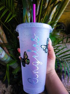 a person holding up a purple cup with butterflies on it