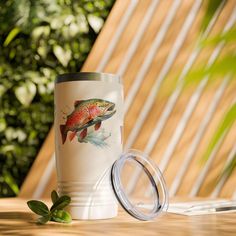 a white coffee cup with a fish on it next to a green leafy plant