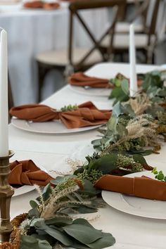 the table is set with white plates and greenery on them, along with candles