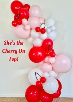 there is a bunch of balloons in the shape of cherrys on top, and one balloon that says she's the cherry on top