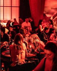 a group of people sitting at tables in a restaurant with red lighting on the walls