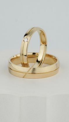 two gold wedding rings on top of each other, with a diamond in the middle