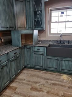 an empty kitchen with wooden floors and blue cabinetry, including a black farmhouse sink